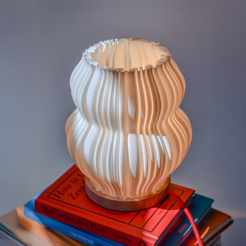 Tischlampe Pæra auf Bücherstapel in wohnlicher Umgebung – geschwungene Form mit verspieltem Lichtspiel